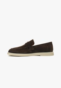Braune Wildlederschlüpfschuhe mit einem flachen Design, abgerundeter Spitze und einer kontrastierenden cremefarbenen Gummisohle. Mit einem dekorativen Riemen.
