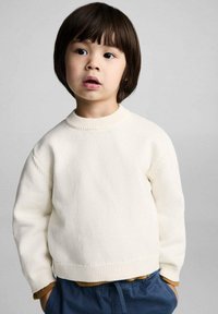 White knitted sweater with a round neckline, long sleeves, and ribbed cuffs, worn over blue drawstring pants. Smooth texture, casual fit.
