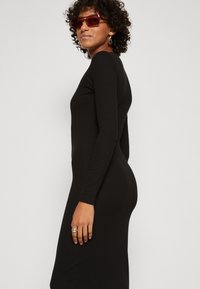 Black long-sleeve dress with a form-fitting silhouette, soft texture, and a crew neck. Paired with oversized red sunglasses and earrings.