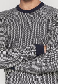 Pletený svetr v námořnické modři a krémové barvě s texturovaným vzorem. Má žebrovaný kulatý výstřih a manžety, představující přiléhavý střih.