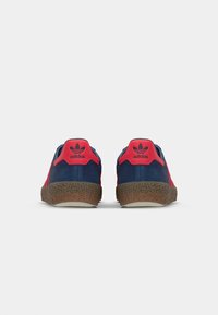 Adidas sneakers med en marineblå overdel, lyserøde accenter, struktureret brun gummisål og logo på hælen. Retro design med mesh-paneler.