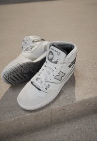 High-top white sneakers with leather and synthetic material, featuring a textured surface, prominent black accent, and "650" logo on the side.