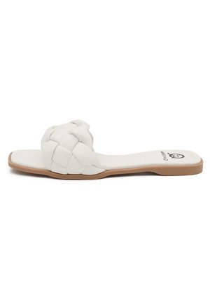 Witte platte slip-on sandaal met gevlochten band en tankleurige zool, zijaanzicht op een witte achtergrond.