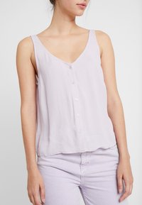 Light lavender sleeveless top made of soft fabric with a V-neck, featuring a button-front closure and a loose, relaxed fit.