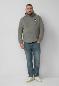 Grauer Kapuzenpullover mit Fronttasche und gesticktem Design, kombiniert mit hellblauen Jeans und weißen Sneakers. Glatte Textur, lockere Passform.