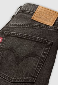 Zwarte spijkerbroek van denim met een achterzak met contrasterende stiksels, een leren label met opgedrukte tekst en een klein rood label aan de zijkant.