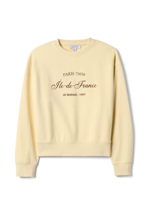 Sudadera amarilla con cuello redondo, texto impreso en marrón: "PARÍS 75056 Île-de-France LE MARAIS - 1997." Puños y dobladillo acanalados.