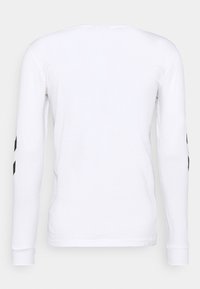 Witte katoenen T-shirt met lange mouwen, een ronde hals en zwarte diagonale accenten op de mouwen. Soepele textuur en aansluitend ontwerp.