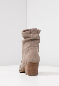 Bottine en daim gris à design décontracté, avec des coutures apparentes et un talon empilé en bois. Vue de dos montrant la tige souple de la bottine.