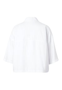 Chemise blanche oversize à manches courtes vue de dos, avec col et coutures d'épaule tombantes, sur un fond uni.
