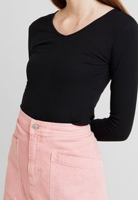 Musta ribattu pitkähihaine paita yhdistettynä vaaleanpunaiseen korkeavyötäröiseen shortsiasukseen, jossa on et pockets ja metallinen napitus.