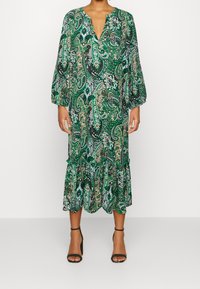 Grön klänning med paisleymönster, djup V-urringning, långa ballongärmar och volangkant. Tillverkad av lättviktsmaterial.