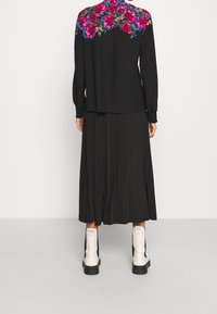 Chemise noire à manches longues avec un imprimé floral vibrant dans le dos, assortie d'une jupe plissée noire et de bottines blanches. 