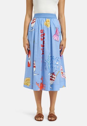 Blaue Midirock mit bunten Prints von Meeresfrüchten, Muscheln, Getränken und Schriftzügen, getragen mit weißem Oberteil und braunen Sandalen.