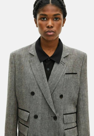 Grau-Hahnentritt-Jacke mit schwarzem Akzenten, doppelter Knopf-Front, eingesetzten Revers und zwei Fronttaschen. Sichtbare Knopfverschlussdetails.