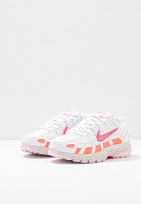 Paire de baskets blanches Nike avec des touches roses et orange, exposée sur un fond clair uni.