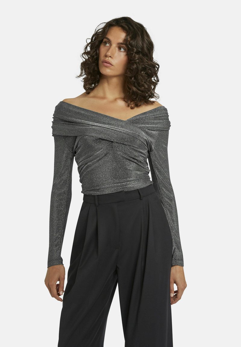 Zilveren off-shoulder top met lange mouwen, met een gedrapeerd ontwerp en subtiele glans, gecombineerd met hoge taille zwarte broeken.