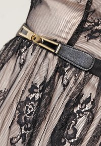 Abito in pizzo nero con intricati motivi floreali, texture trasparente, con una cintura nera e una fibbia dorata come accento.