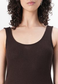 Débardeur marron côtelé avec un décolleté rond et des bretelles larges, fabriqué dans un tissu doux et texturé. Design minimaliste, silhouette ajustée.