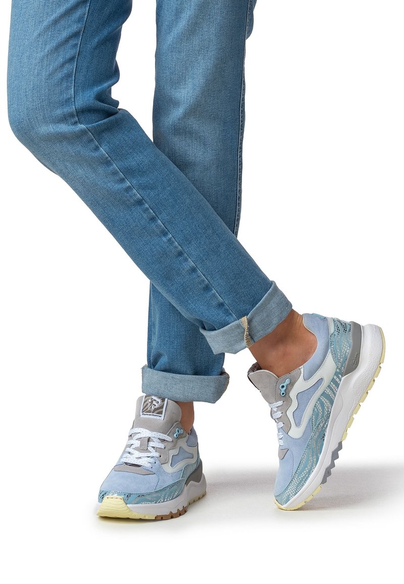 Sneakers azzurro chiaro con tessuto strutturato, design stratificato e dettagli grigi. Suola spessa con un accenno di giallo sul fondo. Denim risvoltato alla caviglia.