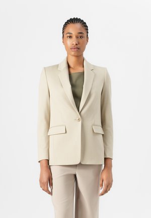 Beige blazer made of smooth fabric with notched lapels, single button closure, and two front pockets, paired with an olive green top.
