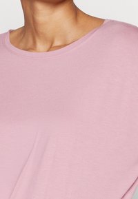 Halenka s výstřihem ve tvaru lodičky a krátkým rukávem ve světlé růžové barvě; měkká textura s volnějším střihem, která má kolem výstřihu jemné prošívání.