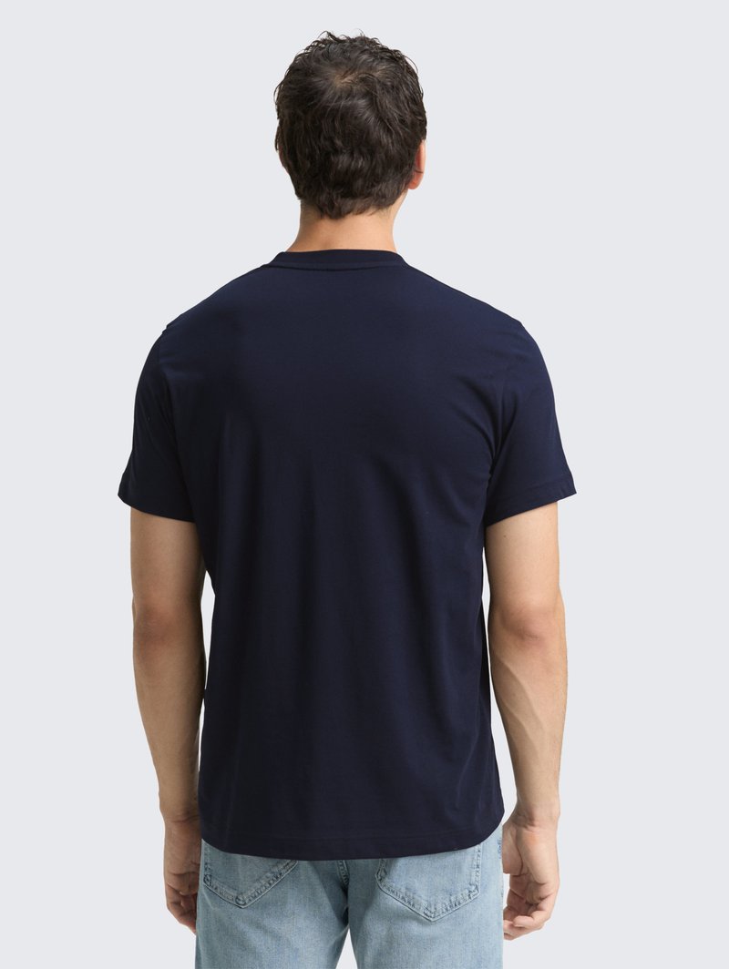 Granatowa bawełniana koszulka z krótkim rękawem i okrągłym dekoltem, przedstawiona z tyłu. W zestawieniu z jasnoniebieskimi dżinsami.