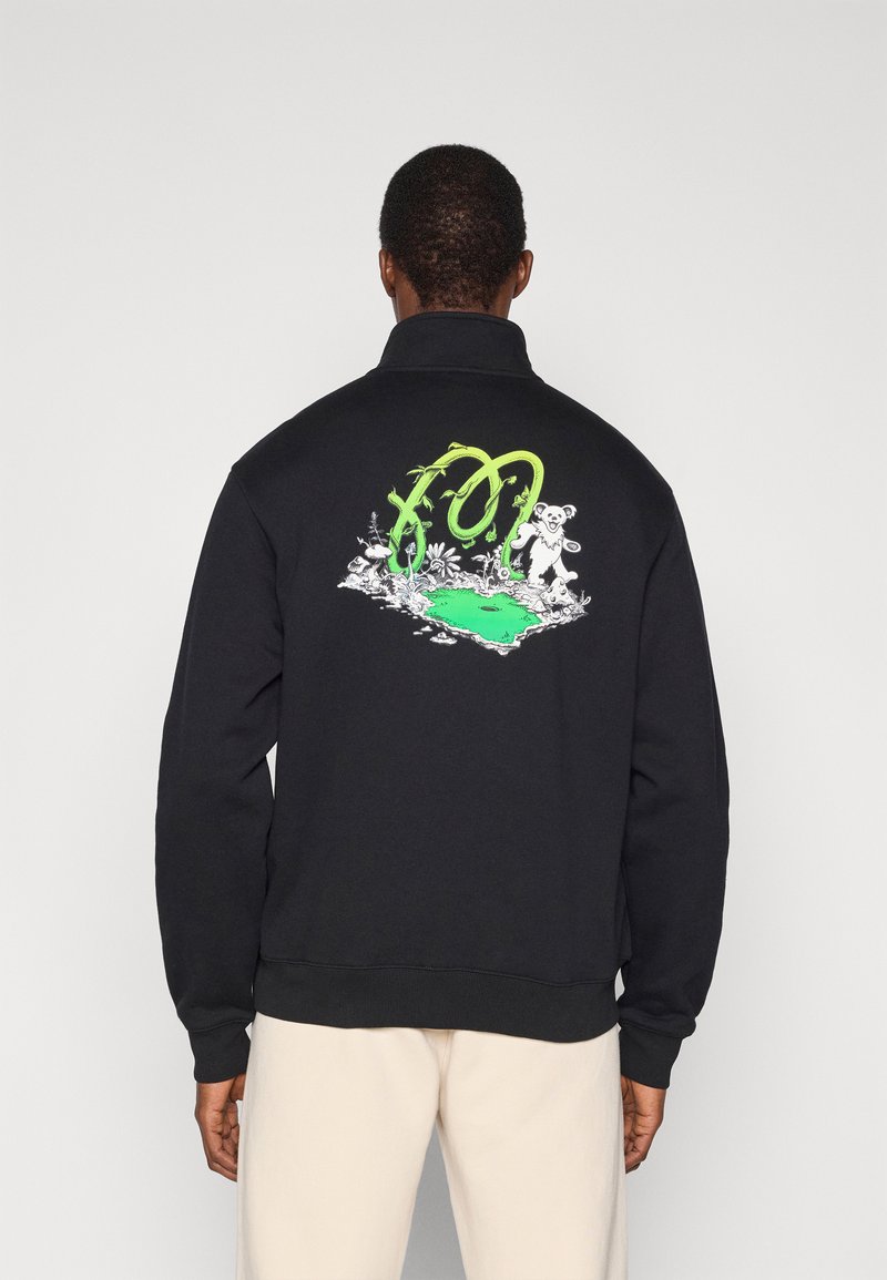 Μαύρο φούτερ με ψηλό γιακά, που διαθέτει πολύχρωμο σχεδιασμό με γραφικά στην πλάτη, περιλαμβάνοντας πράσινες πινελιές και απεικονίσεις ζώων.