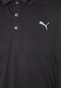 Černé polo tričko z hladké látky s tříknoflíkovou légou a bílým logem Puma na levé části hrudi. Jemně lesklá textura.