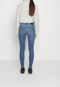 Jeans skinny azules con cintura alta, que cuentan con dos bolsillos traseros y una etiqueta de cuero negro. Combinados con un suéter de punto gris claro.