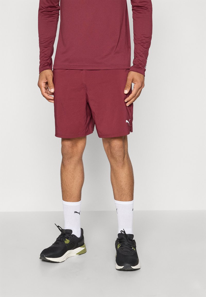 Bordeauxfarbendes Langarmshirt kombiniert mit bordeauxfarbenen Sportshorts. Schwarze Sneakers mit grünen Akzenten und weißen Socken. Sauberes Design, glatte Textur.