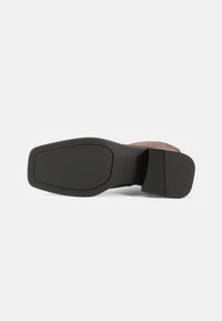 Brune semskede sko med en teksturert svart gummisåle. Sålen er litt avsmalnet, med en rektangulær form og minimale detaljer.