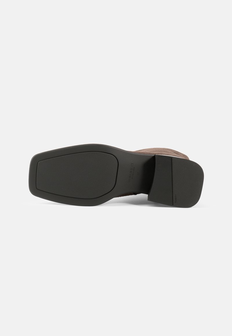 Chaussure en suede marron avec une semelle en caoutchouc noir texturé. La semelle extérieure est légèrement effilée, présentant une forme rectangulaire et un minimum de détails.