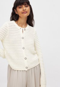 Cardigan en ivoire tricoté avec un motif rayé texturé, col rond et fermeture frontale avec des boutons foncés. Matière douce et légère.