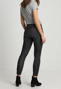 Jeans slim de tiro alto en denim de lavado oscuro, con una textura sutil. Combinados con botas negras hasta el tobillo para crear contraste.