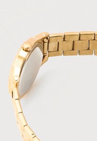 Zlato tonirana ročna ura z brušeno jekleno zapestnico, okroglim ohišjem in gladko kovinsko površino na zadnji strani.