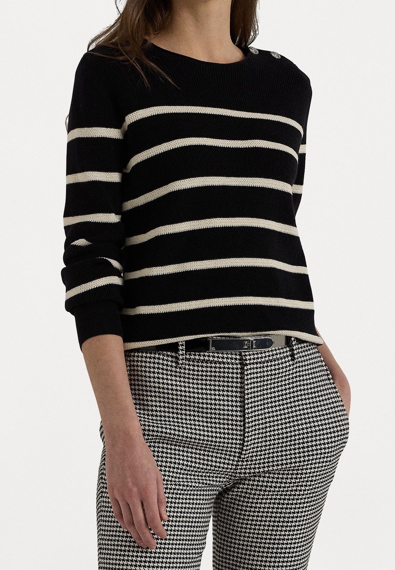 Pull en maille rayé noir et blanc avec manches longues, col rond et boutons décoratifs. Associé à un pantalon à carreaux pied-de-poule.
