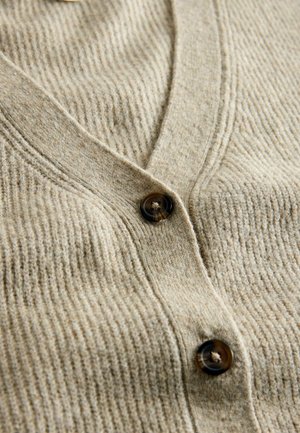 Beige gerippte Strickjacke mit V-Ausschnitt und dunklen braunen Knöpfen. Die Textur ist weich, mit vertikalen Rippungen über den Stoff.