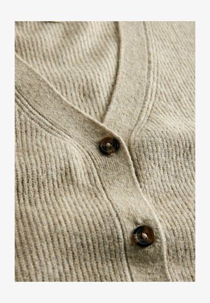 Beige gerippte Strickjacke mit V-Ausschnitt und dunklen braunen Knöpfen. Die Textur ist weich, mit vertikalen Rippungen über den Stoff.