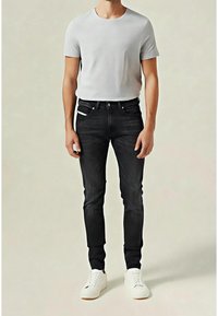 Grå t-shirt med rund halsmatchad med slim-fit svarta jeans och vita sneakers. Anmärkningsvärda detaljer inkluderar kontrastsömmar och fem fickor.