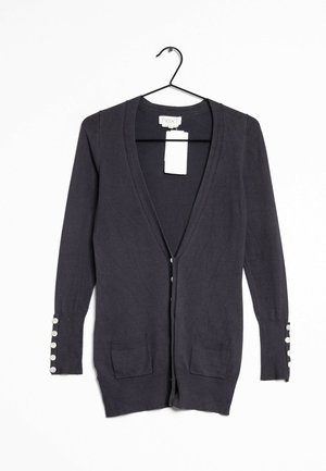 Cardigan bleu marine foncé avec des manches longues, un col en V, deux poches avant et des détails de boutons sur les poignets. Fabriqué en tissu tricot doux.
