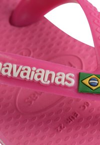 Dettaglio ravvicinato di un cinturino di flip-flop Havaianas rosa che mostra il nome del marchio e il piccolo emblema della bandiera brasiliana su una suola testurizzata.