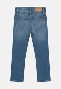 Denim jeans i middels blå vask, med rett ben-kutt, to baklommer og et beige logo-patch på livbåndet.