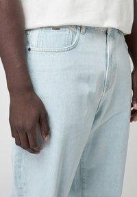 Jasnoniebieskie dżinsy z denimu o luźnym kroju, klasycznym fasonie z pięcioma kieszeniami i subtelnych detalach przeszyć. Materiał wydaje się miękki i lekki.