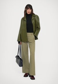 Giacca oversize in pelle verde, dolcevita nero, pantaloni a zampa d'elefante a quadri verde chiaro, borsa nera e scarpe bordeaux. Texture morbide e vestibilità sartoriale.