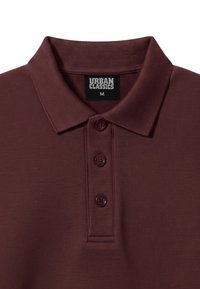 Polo marron foncé avec un col côtelé et trois boutons, avec une étiquette noire indiquant Urban Classics taille M.
