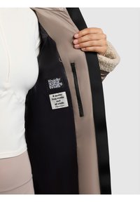 Palton pentru bărbați cu exterior bej și negru, textură interioară moale, buzunar interior, etichete de marcă și compoziție unică a țesăturii pentru căldură.