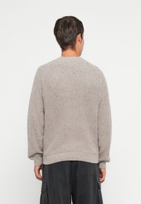 Maglione grigio lavorato a maglia con un design a coste textured, caratterizzato da maniche raglan e scollo rotondo. Il tessuto appare morbido e spesso.