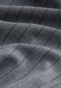 Sötét szürke, texturált szövet finom függőleges tűcsíkokkal. Az anyag sima, enyhén fényes; a redők lágy esést eredményeznek.