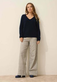 Granatowy sweter z wełny z domieszką, jasnoszare szerokie spodnie z delikatnym wzorem oraz ciemnoniebieskie buty na platformie. Prosty, luźny krój.